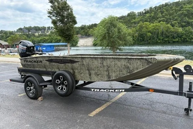 Slide: The Image of 2026 Tracker Grizzly 1650 T Prairie Wings Edition boat on trailer by a scenic river. - 2