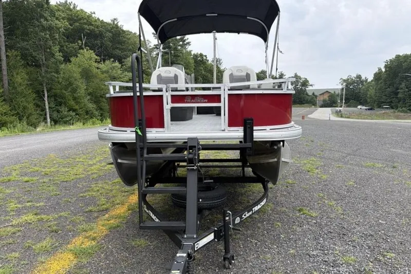 Slide: The Image of 2026 Sun Tracker Bass Buggy 18 DLX pontoon boat on trailer, parked on gravel road. - 9