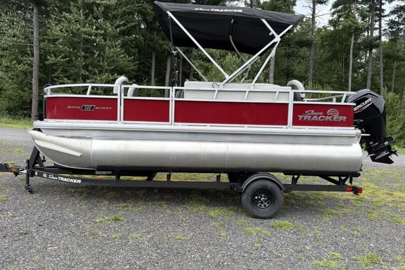 Slide: The Image of 2026 Sun Tracker Bass Buggy 18 DLX pontoon boat on trailer, parked outdoors. - 2