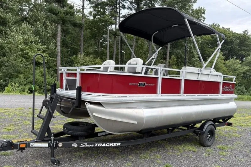 The Image of 2026 Sun Tracker Bass Buggy 18 DLX pontoon boat on trailer, red and silver design. - 0