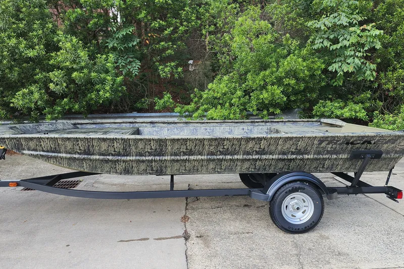 The Image of 2026 Tracker Grizzly 1754 Utility boat on trailer, parked near lush greenery. - 0