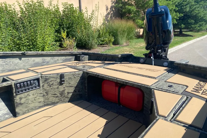 Slide: The Image of 2026 Tracker Grizzly 1756 T Marsh boat interior with camouflage design and motor, parked outdoors. - 4
