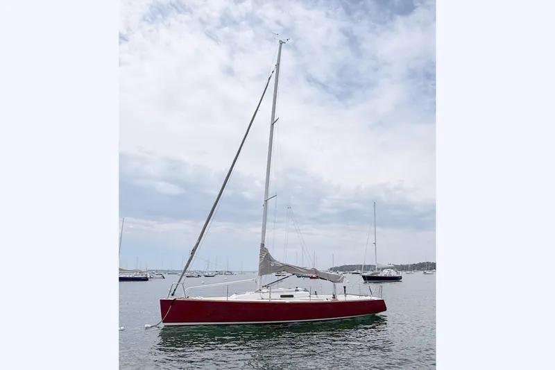 The Image of A red sailboat floating on calm water, featuring a tall mast and cloudy sky. - 0