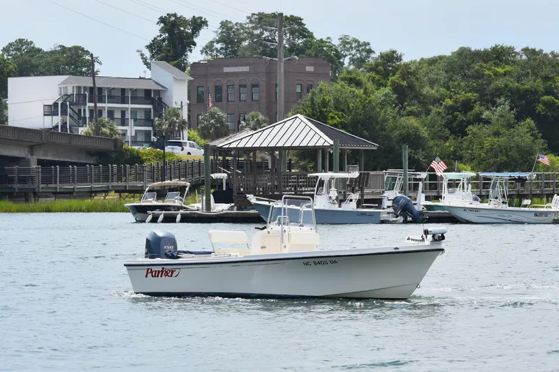 Slide: The Image of 2005 Parker 1801 Center Console boat cruising near a marina with docked boats and buildings. - 1
