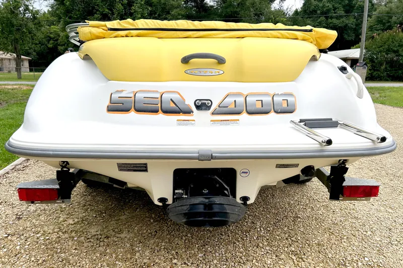 Slide: The Image of 2004 Sea-Doo Sportster LE DI boat rear view with yellow cover on gravel driveway. - 2