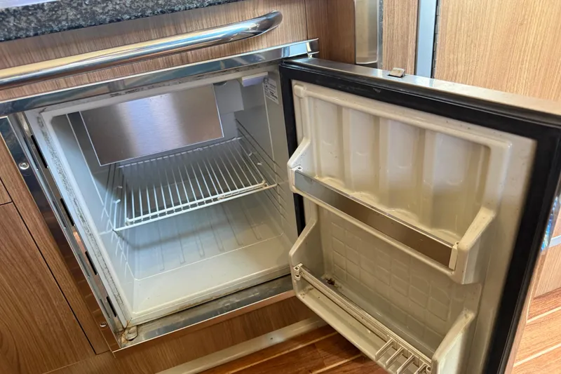 Slide: The Image of Open refrigerator inside 2011 Chaparral 310 Signature boat, showcasing storage space and shelving. - 40