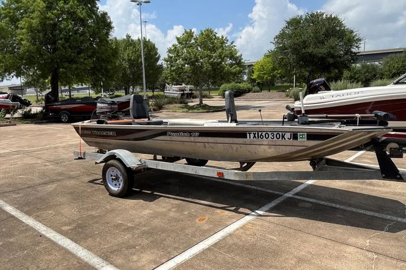 The Image of 2011 Tracker Panfish 16 boat on trailer in parking lot, surrounded by trees and other boats. - 0