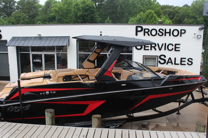 Slide: The Image of 2026 Tigé 24RZX boat in showroom, black with red accents, luxury seating. - 2
