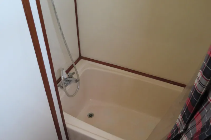 Slide: The Image of Bathtub with shower in 1987 Hershine Aftcabin Motoryacht, featuring wood trim and plaid curtain. - 38