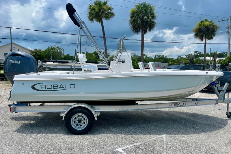 The Image of 2024 Robalo 206 Cayman boat on trailer, parked outdoors with palm trees in background. - 1