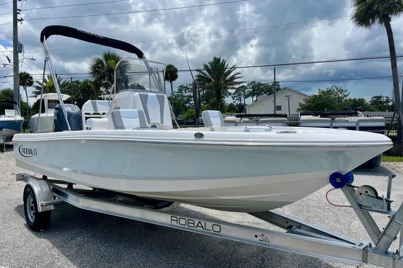 Slide: The Image of 2024 Robalo 206 Cayman boat on trailer, parked outdoors under cloudy sky. - 2