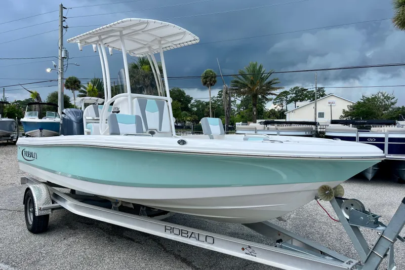 Slide: The Image of 2024 Robalo 206 Cayman boat on trailer, under cloudy sky, in a parking lot. - 2