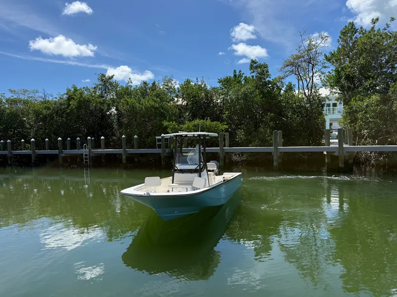 Slide: The Image of A 2027 Boston Whaler 210 Montauk on calm water, surrounded by trees and a dock. - 3