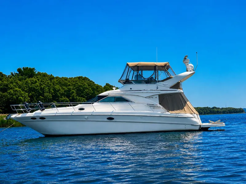 The Image of 2001 Sea Ray 400 Sedan Bridge on calm water, with clear skies and a green shoreline. - 0
