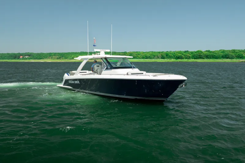 Slide: The Image of 2022 Tiara Yachts 38 LS cruising on open water near a lush green shoreline. - 12