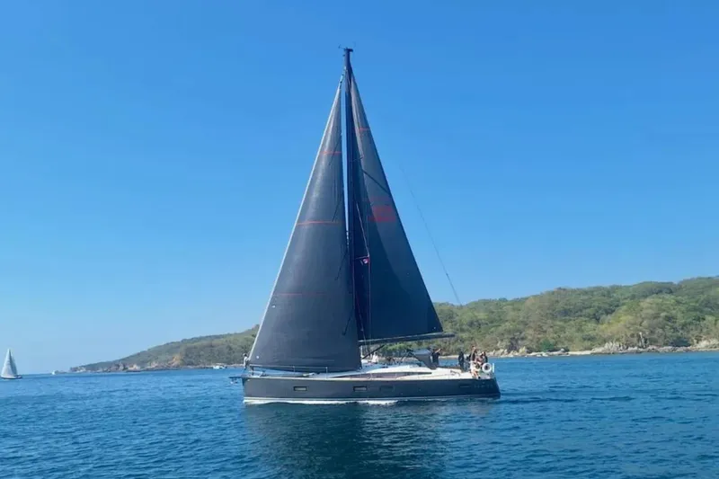 Slide: The Image of 2018 Jeanneau 54 sailboat cruising on calm blue waters near a lush coastline. - 2