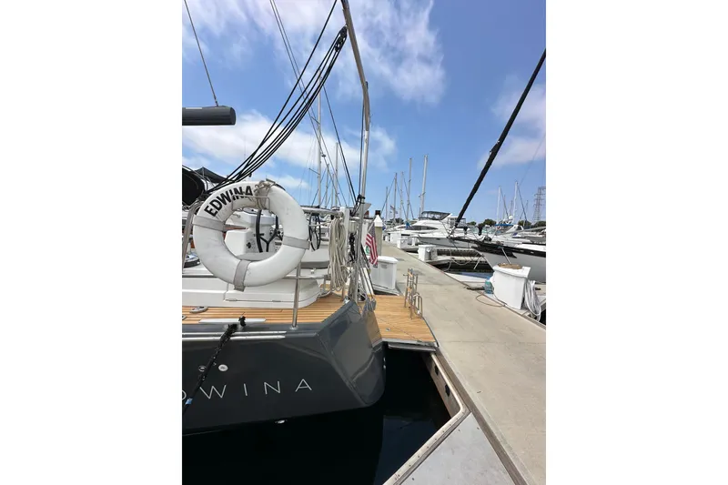 Slide: The Image of 2018 Jeanneau 54 yacht docked at marina, featuring a life ring and clear blue sky. - 19