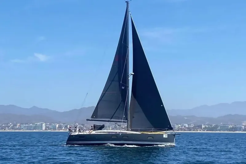 Slide: The Image of 2018 Jeanneau 54 sailboat cruising on calm waters with cityscape and mountains in the background. - 1