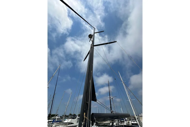 Slide: The Image of 2018 Jeanneau 54 sailboat mast against a cloudy blue sky in a marina. - 53