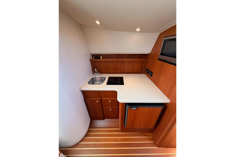 Slide: The Image of Compact galley in 2005 Tiara Yachts 2900 Open Classic, featuring sink, stove, and wood cabinetry. - 48