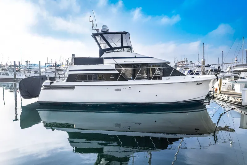 The Image of A 1990 Tollycraft 40 Sport Sedan is docked in the harbor. It features a white hull design and a covered upper deck. - 0