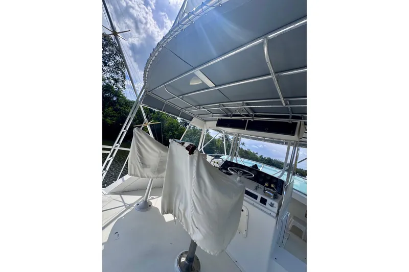 Slide: The Image of 1986 Bertram 46III Convertible boat helm with covered seats and canopy, docked by lush greenery. - 21