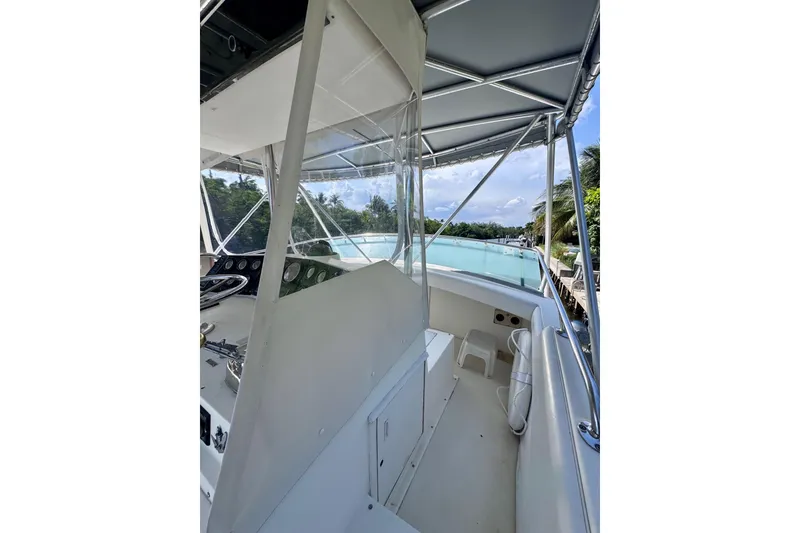 Slide: The Image of 1986 Bertram 46III Convertible boat interior with helm and canopy, docked near lush greenery. - 25