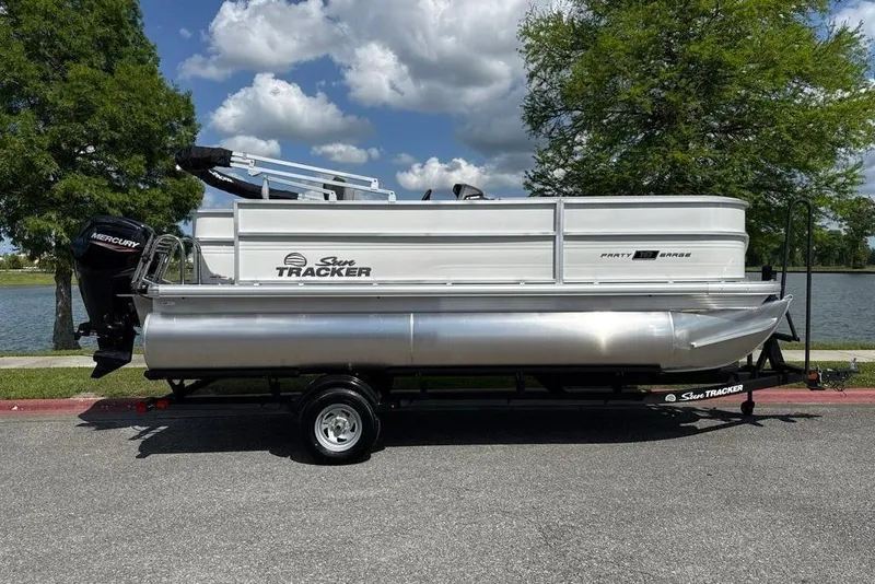The Image of 2026 Sun Tracker Party Barge 20 DLX pontoon boat on trailer by a lake. - 0