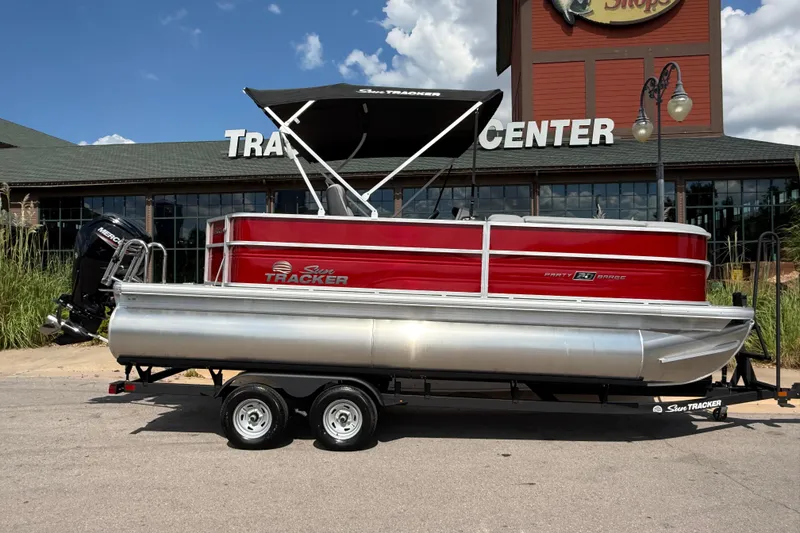 Slide: The Image of 2026 Sun Tracker Party Barge 20 DLX pontoon boat on trailer, parked outside a center. - 9
