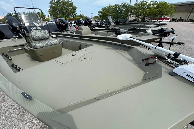 Slide: The Image of 2026 Tracker Grizzly 1860 CC boat with camo seating and trolling motor in a parking lot. - 6