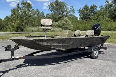 The Image of 2026 Tracker Grizzly 1860 CC boat on trailer, parked outdoors with lush greenery background. - 0