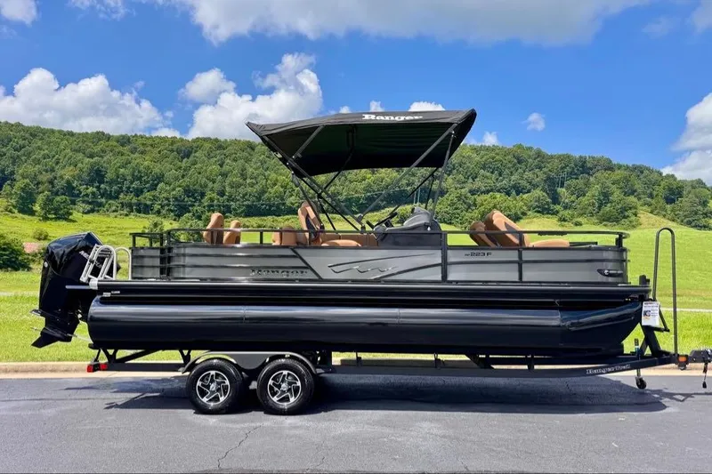 Slide: The Image of 2026 Ranger 223F pontoon boat on trailer, set against a scenic green landscape. - 2