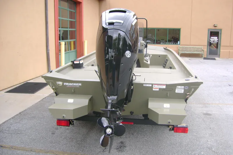 Slide: The Image of 2026 Tracker Grizzly 1860 CC boat with outboard motor, parked outside a building. - 6