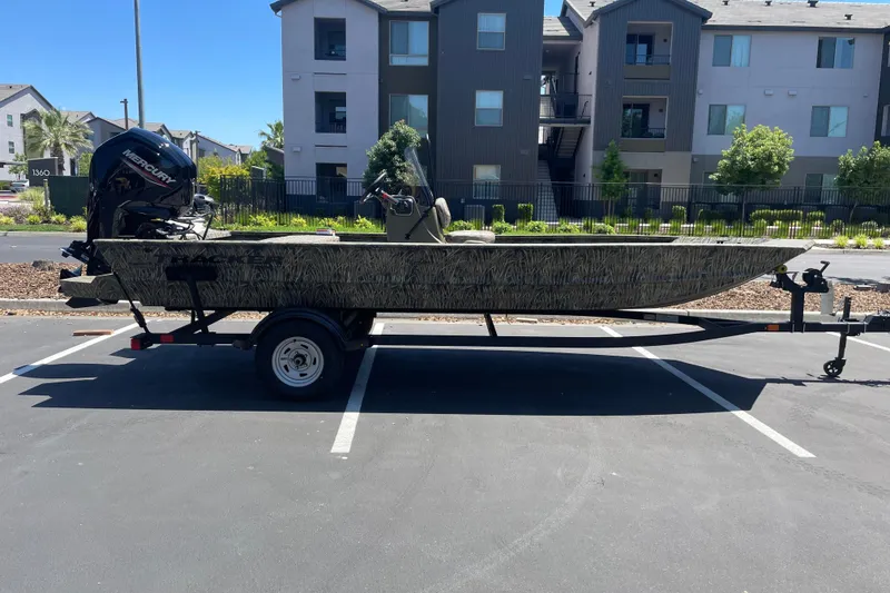 Slide: The Image of 2026 Tracker Grizzly 1860 CC boat on trailer in parking lot, with Mercury outboard motor. - 2