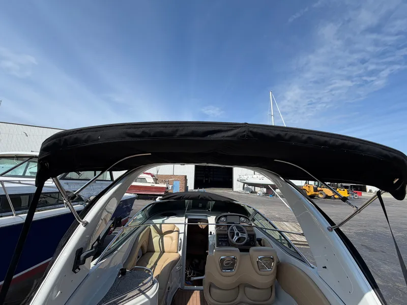 Slide: The Image of 2018 Crownline 264 CR with open cockpit, beige interior, and black canopy, parked outdoors. - 5
