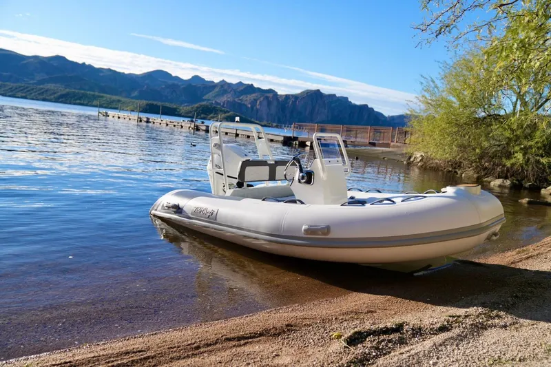 The Image of 2027 Tide Craft San Juan 11 Hypalon boat on a scenic lakeshore with mountains. - 0