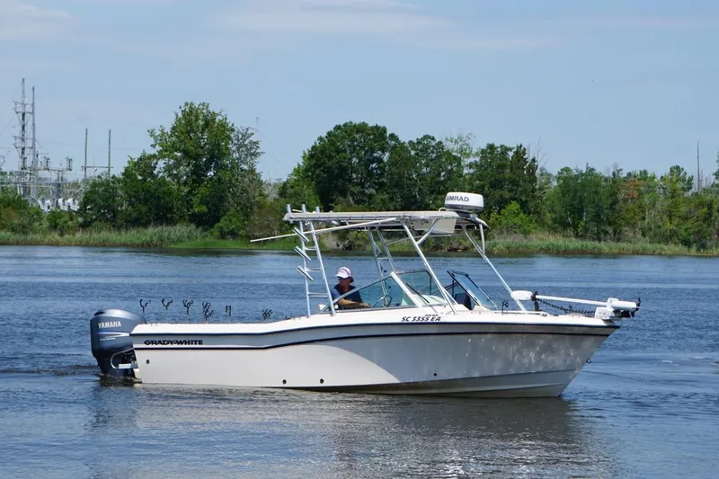 The Image of 1999 Grady-White Tournament 225 boat cruising on a calm river with lush greenery. - 1