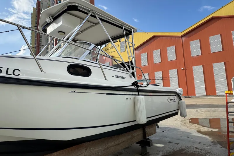Slide: The Image of 1999 Boston Whaler 21 Conquest boat docked near industrial buildings under a clear sky. - 2