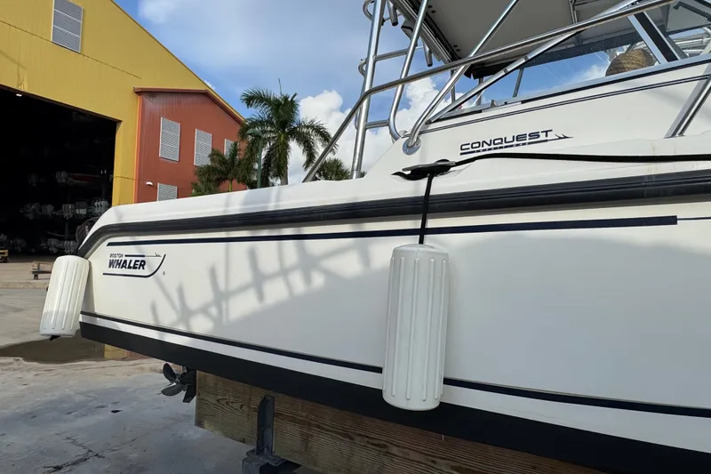 Slide: The Image of 1999 Boston Whaler 21 Conquest boat docked near a colorful warehouse and palm trees. - 3