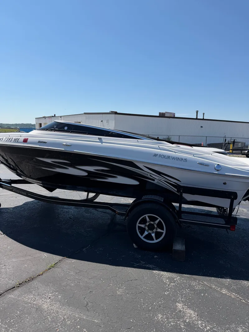 Slide: The Image of A black and white Four Winns motorboat is on a trailer in a parking lot. - 0