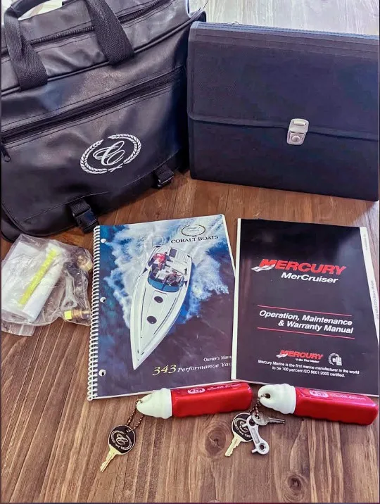 Slide: The Image of Accessories for a Cobalt 343 boat, including manuals, keys, and bags, on a wooden table. - 13