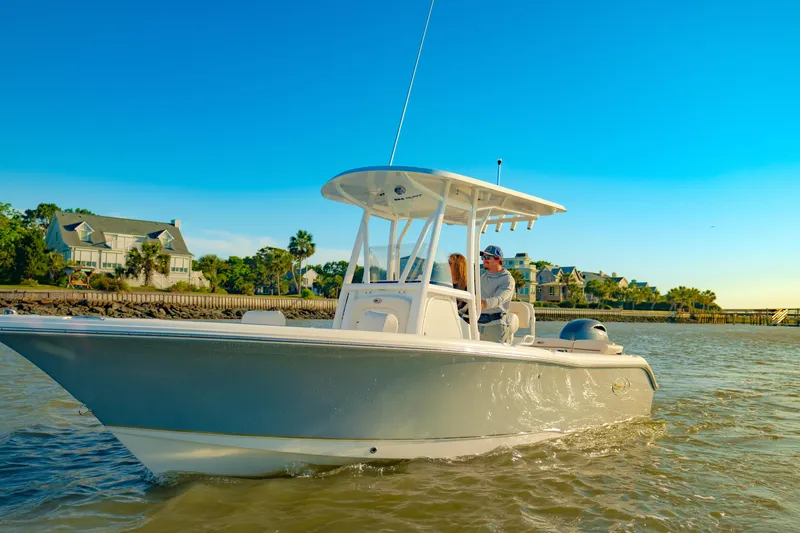 Slide: The Image of 2027 Sea Hunt Ultra 219 boat cruising near coastal homes under clear blue sky. - 38