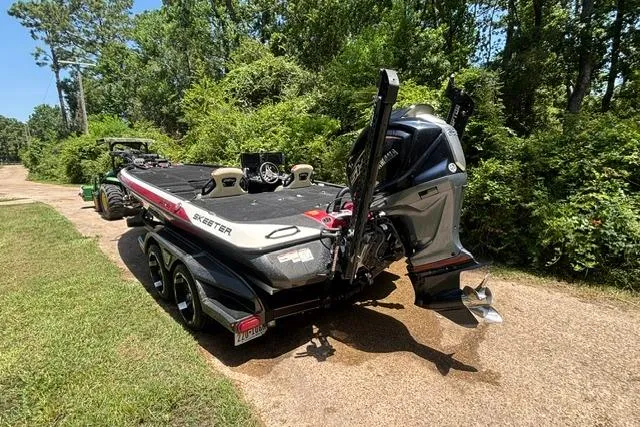 Slide: The Image of 2022 Skeeter FXR21 Limited boat on trailer, parked on a sunny, tree-lined path. - 2