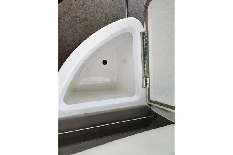 Slide: The Image of Storage compartment in a 2005 Cobalt 250 boat, featuring a hinged lid and drain hole. - 18