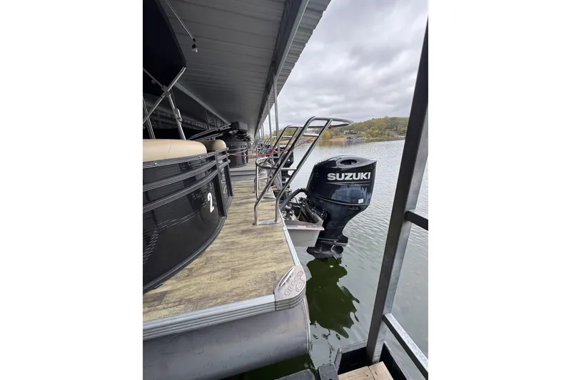 Slide: The Image of 2023 Crest Classic LX 220 pontoon boat with Suzuki outboard motor docked on a lake. - 2