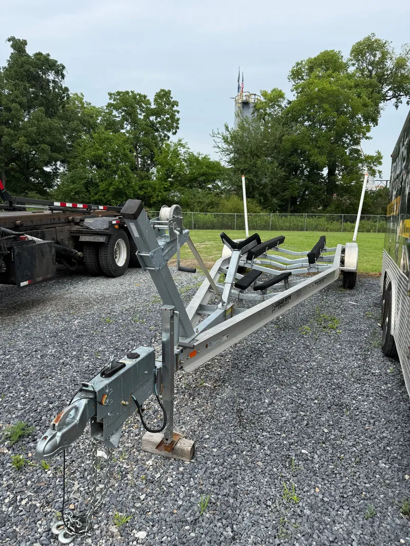Slide: The Image of A boat trailer sits on a gravel lot, surrounded by trees and trucks. - 14