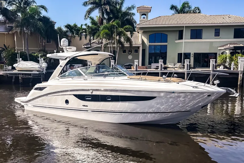 Slide: The Image of 2016 Sea Ray Sundancer 350 yacht docked by waterfront homes, surrounded by palm trees. - 2