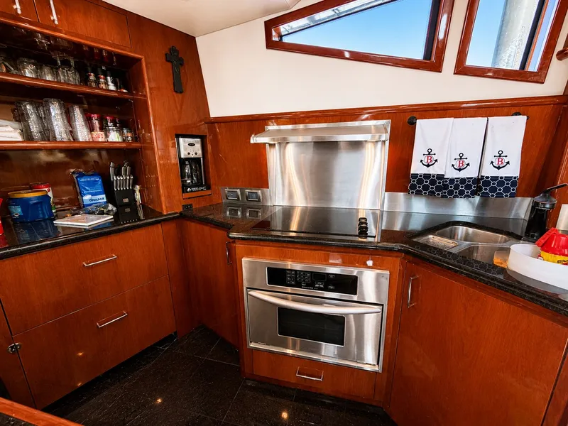 Slide: The Image of The galley of a 2006 Marquis 65 with wooden cabinets, stainless steel appliances, and nautical-themed towels. - 9