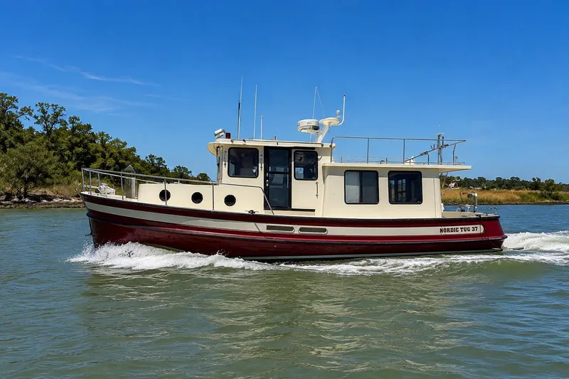 Slide: The Image of 2000 Nordic Tug 37 cruising on a sunny day, surrounded by lush greenery. - 2