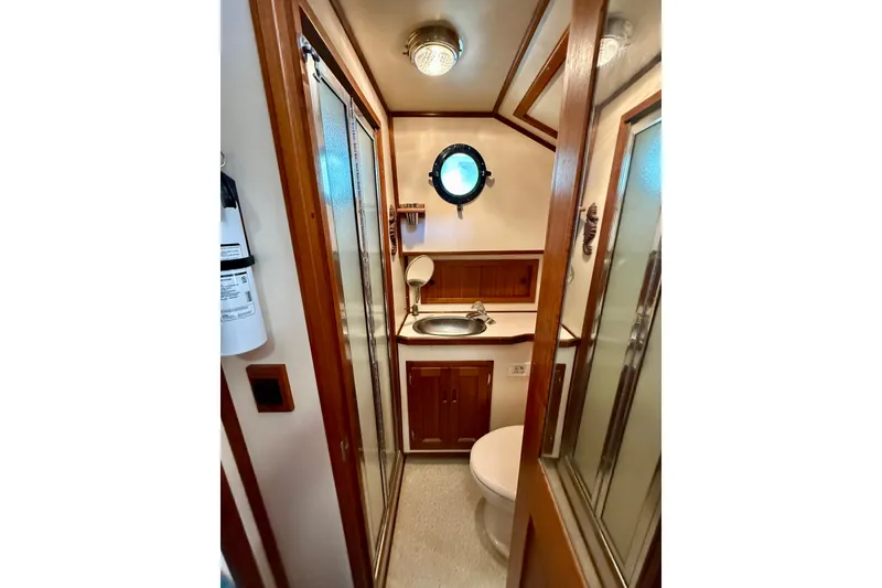 Slide: The Image of Compact bathroom in a 2000 Nordic Tug 37, featuring wood accents and a porthole window. - 50